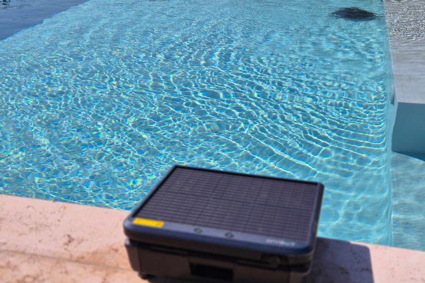 WYBOT S3 Solar-Kit und Dockingstation am Beckenrand. Im Hintergrund reinigt der Poolroboter den Einbaupool.